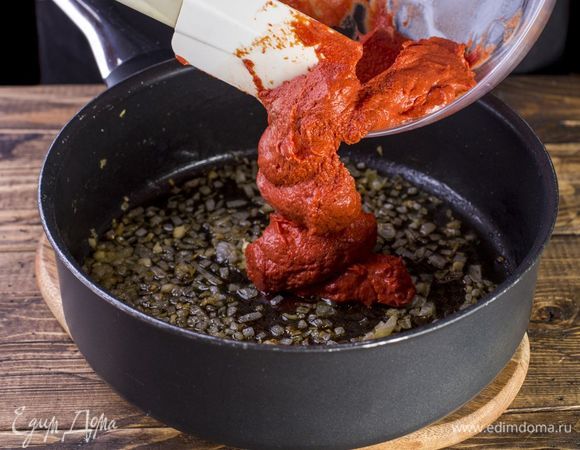 Добавьте пасту к луку с чесноком. Получившийся соус доведите до кипения.