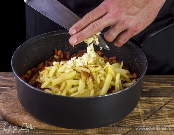 Почти готовый картофель переложите к мясу. Добавьте мелко нарубленный чеснок. Тушите еще пять минут.