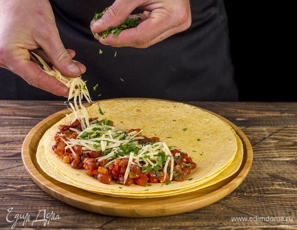 На половину лепешки выложите начинку. Поверх начинки посыпьте сыр и зелень.