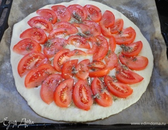 К этому времени тесто увеличится втрое. Раскатайте его прямо на бумаге для выпечки, слегка посыпанной мукой. Помидоры тонко нарезать и выложить по кругу. Сверху полить смесью масла, чеснока, майорана и соли.