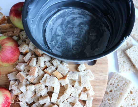 Обрезки хлеба разрежьте на небольшие кубики. Подсушите их в духовке при 180°C. Нам потребуется 1 горсть подсушенного хлеба.<br />
Перед выпеканием шарлотки надо сбрызнуть хлеб растопленным сливочным маслом (10 г). Борта формы обильно смазать сливочным маслом. Хорошо смазать маслом (15 г) бумагу для выпечки, которой следует застелить дно формы.