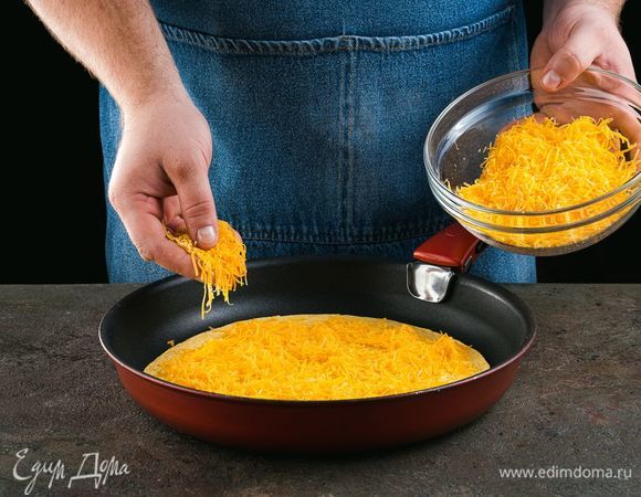 Помойте листья салата. Сыр натрите на терке. Лепешку положите на разогретую сковороду, выложите на нее половину тертого сыра.  