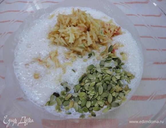 К подошедшим дрожжам добавьте остальной сахар, соль. Отложите 1 ст. л. тыквенных семечек для посыпки (в оригинале были семена подсолнуха), остальные высыпьте в жидкость. Туда же добавьте 1 натертое яблоко. Я взвесила его — 180 г. Все перемешайте.