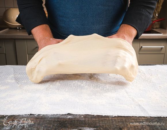 Достаньте из холодильника тесто, положите на полотенце, посыпанное мукой, и растяните по всей длине полотенца.