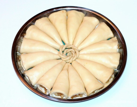 Берем форму для выпечки диаметром 26 см и застилаем пекарской бумагой или силиконовым ковриком. Смазываем холодным сливочным маслом. Выкладываем заготовки по кругу.