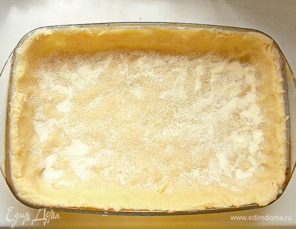 Достаньте тесто из холодильника и распределите ровным слоем по дну и бортикам формы. Посыпьте дно манной крупой.