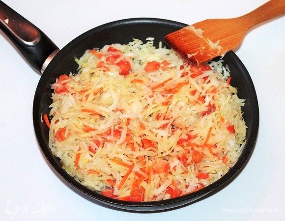 К капусте добавляем лук (1/2 часть), нарезанную соломкой морковь и нарезанный помидор без шкурки. Тушим и периодически перемешиваем. В течение готовки добавляем немного бульона, приправу, солим и перчим. Доводим овощи до полуготовности.