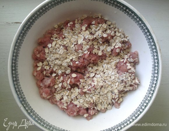 В фарш (у меня свино-говяжий) добавить геркулес и воду. Тщательно перемешать и дать постоять 10–15 минут.
