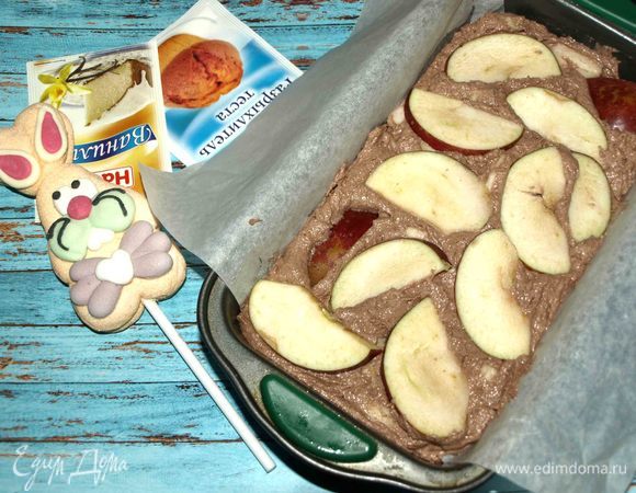 Форму для кекса смазать маслом, выстелить пекарской бумагой, чтобы края свисали по бокам (так удобней извлекать кекс). Перекладываем тесто. И сверху хаотично выкладываем яблоки, нарезанные дольками.