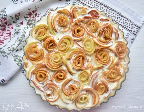 По периметру пирога распределить цветочные заготовки. Вокруг каждой заготовки распределить оставшиеся яблочные ломтики, формируя цветы и одновременно заполняя пустоты между ними. Сверху яблоки посыпать тростниковым сахаром.