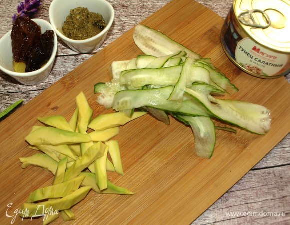 Пока варятся макароны, подготовить овощи. Половину авокадо нарезать дольками. Огурец нарезать тонкими полосками при помощи овощерезки. Вяленые помидоры нарезать, зеленый лук мелко порубить. Сыр измельчить на терке.