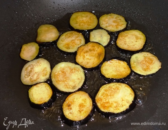 С баклажанов слить жидкость, обсушить кружки бумажным полотенцем. Разогреть 3 ст. л. растительного масла и обжарить на нем баклажаны с обеих сторон до румяности.