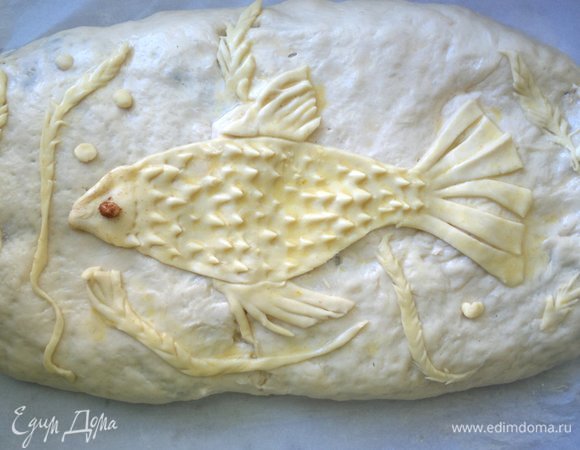 На поверхность кулебяки выложить все подготовленные детали. С помощью ножниц сделать рыбе чешую, затем смазать детали яйцом с водой. Дать постоять еще минут 20. Затем поставить противень в духовку, разогретую до 180°C, на 40–45 мин.