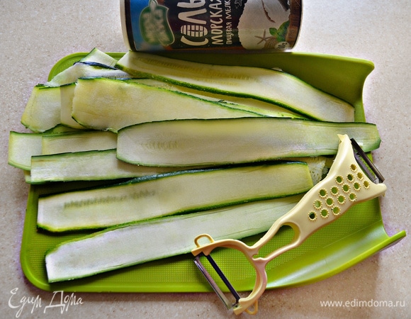 Цукини (у меня два небольших) нарежьте на длинные тонкие ломтики. Для этого лучше использовать овощечистку. Слегка посолите и поперчите.