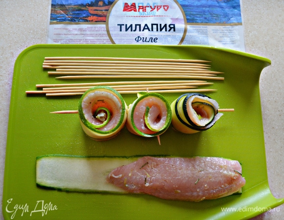 Шпажки замочите в воде на 15–20 минут. После чего разложите полоски цукини, сверху уложите кусочки филе рыбы, плотно сверните и нанизывайте по 3 штуки на шпажки.