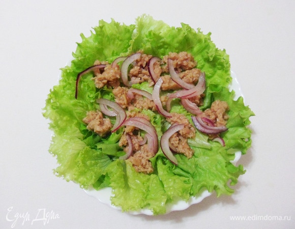 Салатные листья порционно разложить по тарелкам. Сверху положить кусочки консервированного тунца и маринованный лук.