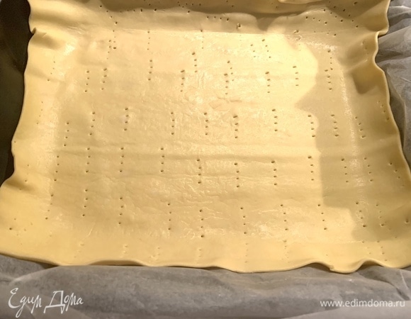 Готовое слоеное тесто разложить, отрезать один кусок шириной примерно 5–7 см для того, чтобы накрыть сверху пирог лентами из этого теста. Оставшийся пласт кладу на противень, прокалываю в нескольких местах вилкой. Духовку разогреваю до 190°C.