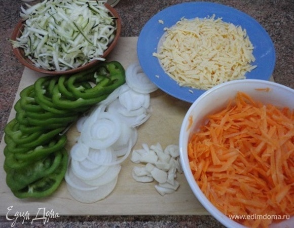 Нарезать лук, перец любого цвета и чеснок тонкими кольцами или пластинками. Морковь, кабачки и сыр натереть на крупной терке. Зелень порубить. Разогреть духовку до 200–220°C.