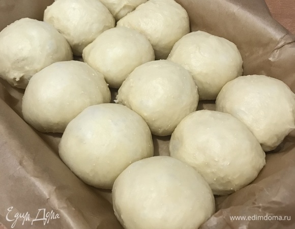 Поднявшееся тесто вымесить и разделить на 12 частей. Сформовать круглые булочки и выложить их в форму для выпечки, застеленную пергаментной бумагой.