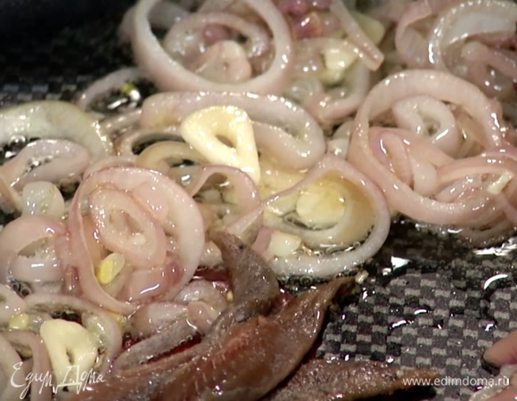 Чеснок измельчить, высыпать к луку. Туда же добавить анчоусы, продолжить обжаривать.