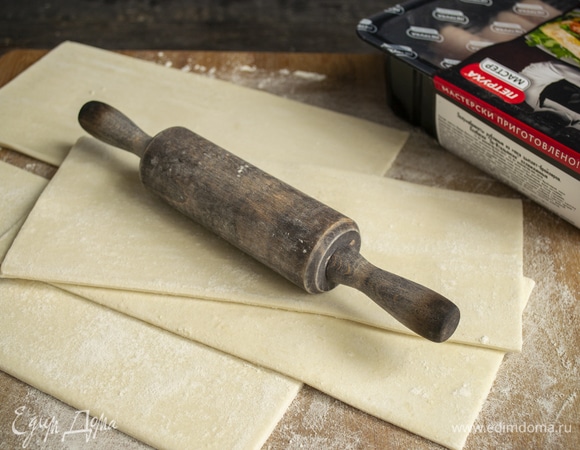 Замороженное слоеное тесто выкладываем на рабочую доску, присыпанную мукой, оставляем на 20 минут. Тем временем готовим начинку. Для ускорения процесса сразу включаем духовку, нагреваем до 200°C.