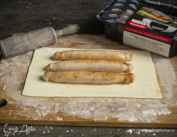 На неразрезанный лист теста кладем остывшие колбаски, нужно по 3 штуки на 1 пирожок.
