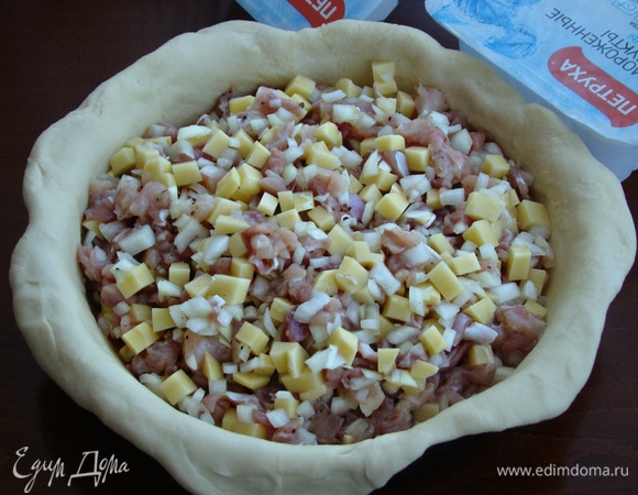 Тесто еще раз вымесить и разделить на две части — большую и чуть поменьше. Большую часть тонко раскатать в круг. Он должен быть больше формы для запекания. Форму смазать растительным маслом и тесто аккуратно уложить в форму так, чтобы края теста свисали по краям формы. В середину равномерно выложить начинку. Форму для пирога лучше взять с высокими неразъемными бортиками.