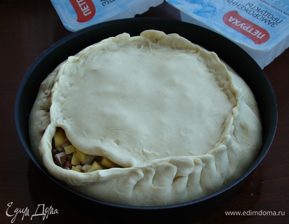 Вторую часть теста разделить еще на две равные части. Одну часть тонко раскатать в круг диаметром меньше, чем форма для запекания, и этот круг уложить поверх начинки. Края по кругу защипнуть.