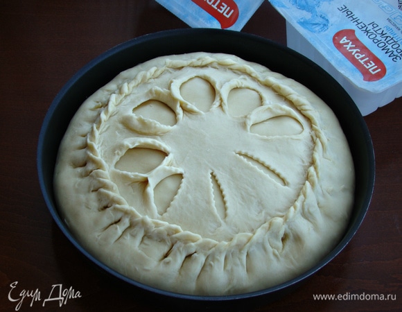 Оставшуюся часть теста тонко раскатать и сделать 8 разрезов, не доходящих до края. Этот круг уложить сверху пирога и тщательно защипнуть края по кругу. Разрезы закрепить в виде узора.