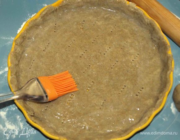 Тесто раскатываем в пласт. Распределяем в форме (моя 26 см в диаметре), формируем бортики, лишнее обрезаем. Прокалываем пласт вилкой, смазываем оставленным белком. И отправляем в заранее разогретую до 180ºС духовку на 5–10 минут. Белок запечатает тесто и не даст ему раскиснуть от начинки.