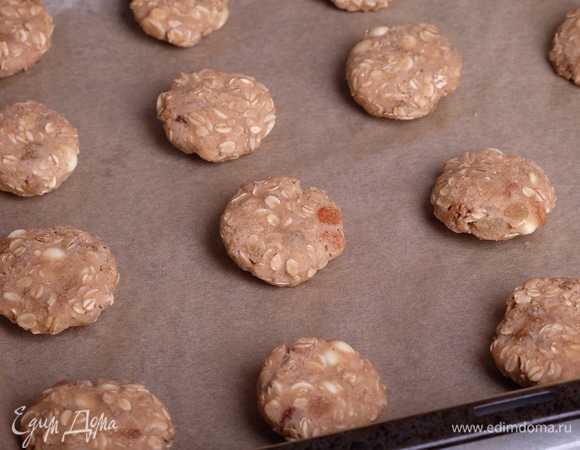 Духовку разогреть до 180°C. От охлажденного теста отламывать небольшие кусочки, скатать шарики величиной примерно с грецкий орех, слегка расплющить их и уложить на противень, покрытый бумагой для выпечки, на большом расстоянии друг от друга.