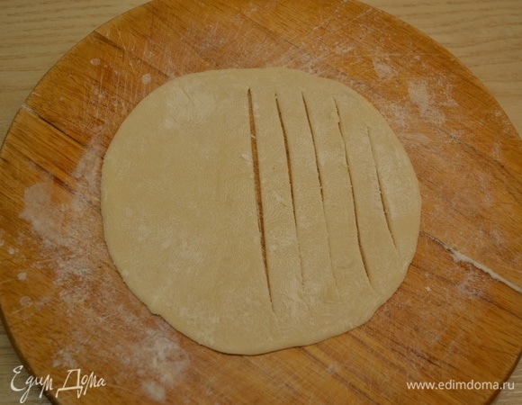 Тесто поделить на 15 кусочков, каждый кусочек скатать в шарик, а затем раскатать в лепешку. Тесто в процессе можно подпылять мукой. На одной половине лепешки сделать надрезы. Вторую половину слегка смазать водой.