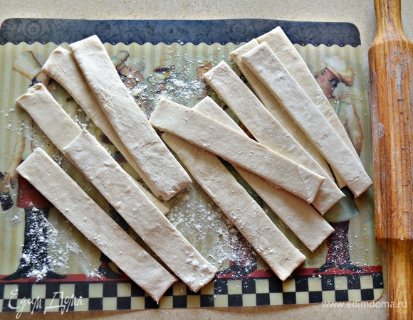 Тесто разморозьте, положите на припыленную мукой поверхность и разрежьте на три полоски размером 24 х 7,5 см. Затем уложите полоски друг на друга и разрежьте на 12 частей шириной 2 см.