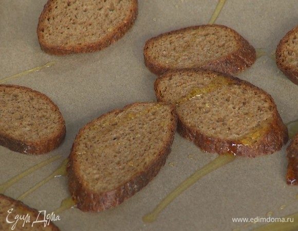 Хлеб нарезать на ломтики, выложить на противень, сбрызнуть оливковым маслом. Поставить в духовку на режим «гриль», поджарить до хрустящей корочки.