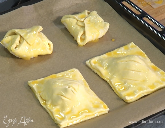 Выложить слойки на противень, застеленный пергаментной бумагой. Выпекать в предварительно разогретой до 200°С духовке в течение 15 минут.