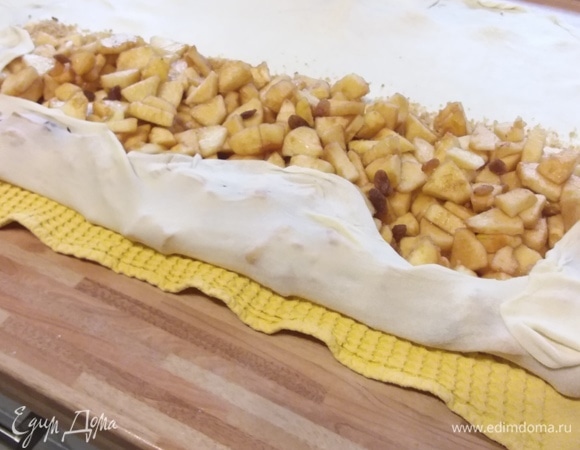 На половину теста высыпать сухарную крошку, оставить свободный ранд. На крошку выложить яблоки (сок, выделившийся от яблок, необходимо удалить). С помощью полотенца свернуть в рулет, загибая края.