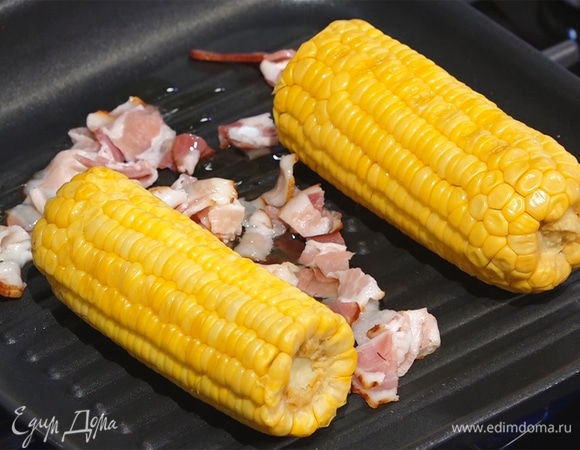 Бекон нарезать тонкими полосками, выложить на сковороду к кукурузе, полить растительным маслом.