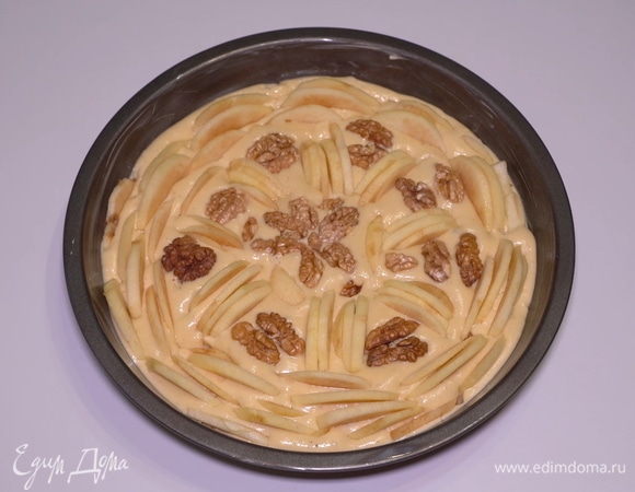 После этого аккуратно распределяю дольки яблок. Не укладываю горизонтально, а именно вставляю вертикально в тесто и еще слегка втапливаю сюда кусочки грецких орехов. Ставлю вкуснятину в предварительно разогретую до 180°C духовку на 30–35 минут, готовность проверяю шпажкой.