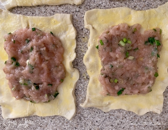 Тесто разрезать на порционные кусочки. Фарш — на середину, края по периметру смазать желтком.