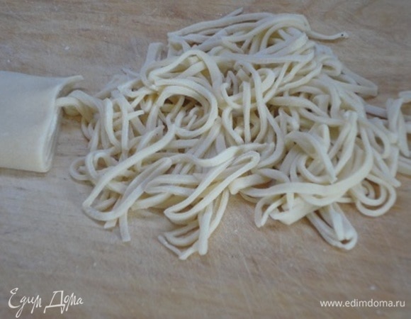Пока готовится бульон, из воды, яйца, соли и муки замесить крутое тесто. Вымешивать 15–20 минут до эластичности. Затем накрыть влажной тканью или чашкой и дать постоять 15–20 минут. Раскатать в тонкую лепешку, подсушить таким образом, чтобы она оставалась эластичной, не ломалась. Свернуть трубочкой и нарезать во всю длину лепешки лапшу шириной 0,5 см.