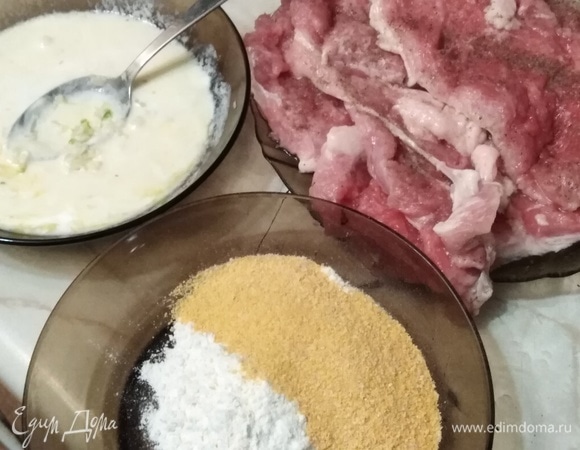 Мясо нарезать на порционные куски примерно по 100 г. Отбить с двух сторон. Посолить, поперчить. Сметану смешать с яйцом. Добавить измельченный чеснок. Муку смешать с панировочными сухарями.