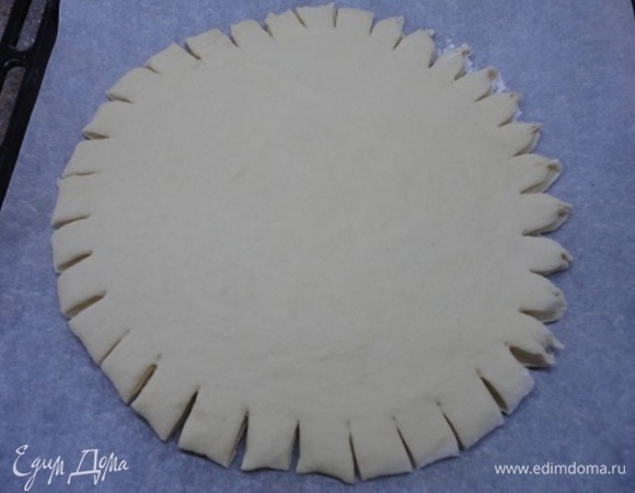 Основу раскатываем в круг прямо на бумаге для выпечки, посыпанной мукой. Стараемся сформировать круг, делаем надреза и защипываем их.