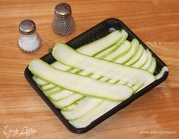 Кабачки разрезаем по всей длине на пластины толщиной в 5–7 мм и солим. Оставляем на 15 минут в сторону. Включаем духовку нагреваться до 180°C.