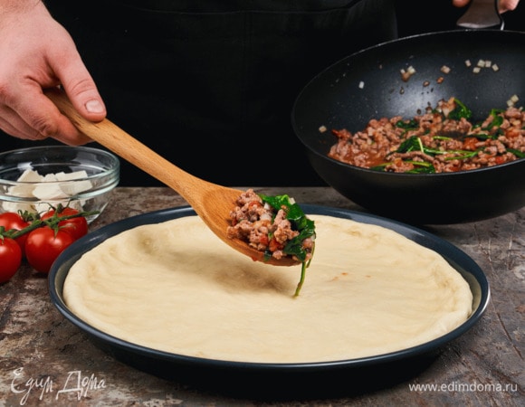 Раскатайте тесто в круг, который будет шире диаметра вашей формы. Выложите тесто в предварительно смазанную сливочным маслом форму, сформировав бортики. Выложите начинку и томаты черри. Сверху выложите кусочки феты. Края теста заверните и смажьте оливковым маслом.