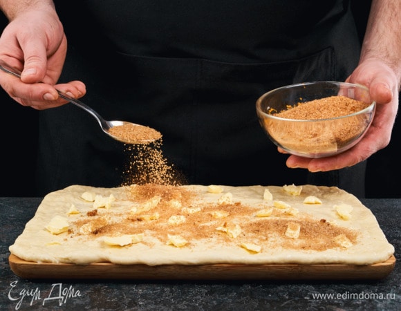 Обомните подошедшее тесто и тонко его раскатайте в прямоугольник. Смажьте его размягченным сливочным маслом, посыпьте сахаром с корицей.