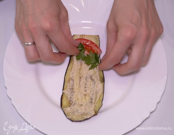 Выкладываю на остывшую баклажанную пластинку 1 ч. л. начинки. Кладу сюда кусочек помидора и веточку петушки. Аккуратно сворачиваю рулетиком.