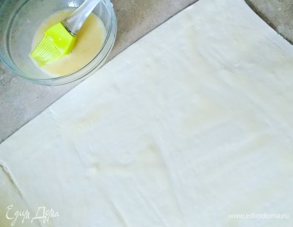 Готовое слоеное тесто немного раскатаем и смажем яйцом.
