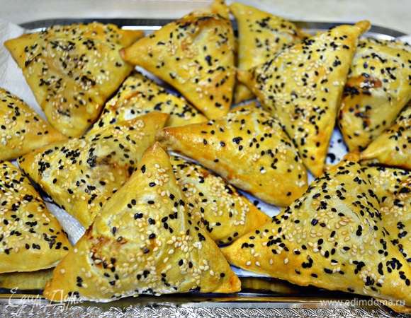 Выложите самсу на противень швами вниз, смажьте взбитым яйцом и присыпьте кунжутом. Выпекайте самсу в разогретой до 180°C духовке около 40 минут. Готовность проверяйте, ориентируясь по своей духовке.