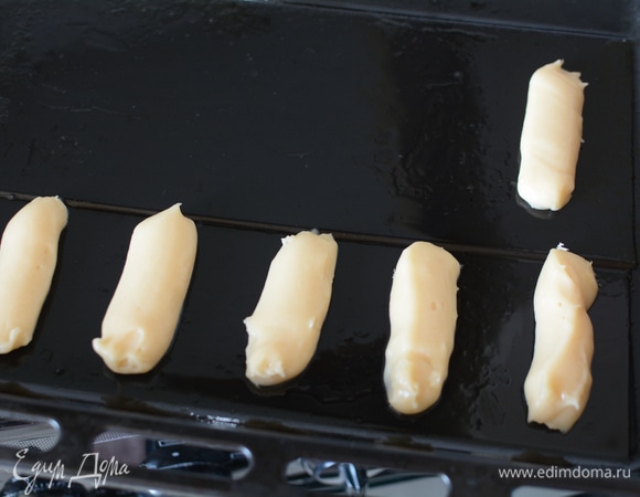 Из кондитерского мешочка на смазанный маслом лист выпускать небольшие колбаски толщиной в мизинец и длиной 5–6 см. Только нужно оставлять зазоры между колбасками. Эклеры при выпечке сильно увеличиваются в объеме. Если выложить плотно, они склеятся между собой. Если кондитерского мешочка не окажется, то можно взять обычный полиэтиленовый мешочек для пищевых продуктов и отрезать один из уголков. Я так и сделала.