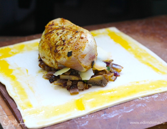 Духовку разогреть до 200°С. Раскатать квадрат теста, длина стороны должна составлять около 18–20 см (с краю можно отрезать тонкую полоску для украшения и вырезать из нее листики, веточки, грибочки). Взбить желток с 1 ст. л. воды, смазать им края квадрата теста. В центр выложить обжаренный лук (площадь расположения начинки прикиньте, исходя их размера филе, оно должно укладываться на начинку как на подушку), на лук выложить слой грибов с петрушкой, на грибы — сыр. Поверх начинки — куриное филе. Сыр можно брать любой, но лучше текучий. Я взяла напополам горгонзолу и сулугуни, нарезала тонкими слайсам.